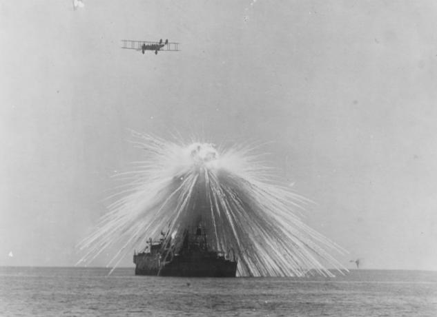 Ένα πλοίο χτυπά με μια βόμβα ενώ ένα αεροπλάνο πετάει πάνω.