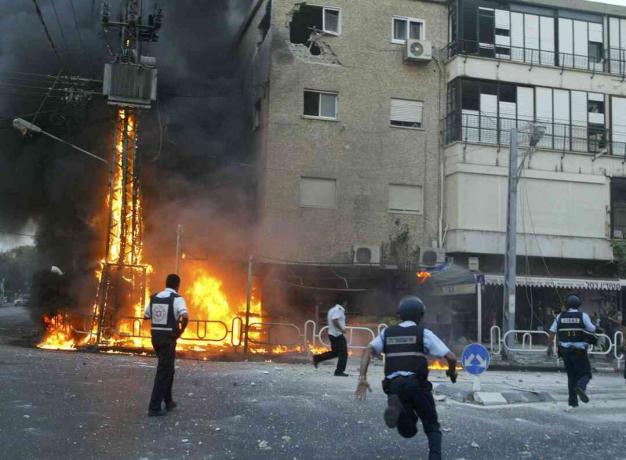 Ισραηλινοί αστυνομικοί σπεύδουν στη σκηνή ενός πυλώνα πυρκαγιάς ηλεκτρικού ρεύματος και κατέστρεψαν τις οικοδομικές στιγμές μετά από μια ρουκέτα της Χεζμπολάχ χτύπησε στις 13 Ιουλίου 2006 στη βόρεια πόλη Nahariya του Ισραήλ.