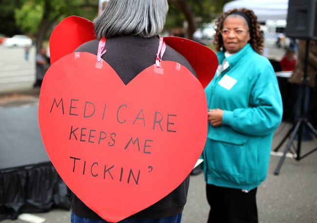 Γυναίκα που φορά μια πινακίδα σε σχήμα καρδιάς που γράφει " Medicare Keeps Me Ticking"