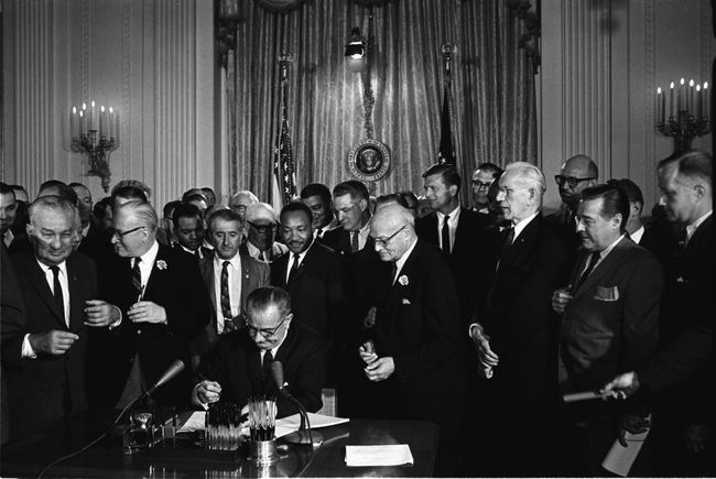 Πρόεδρος Λίντον Β. Ο Τζόνσον υπογράφει τον Νόμο για τα Πολιτικά Δικαιώματα του 1964 καθώς ο Μάρτιν Λούθερ Κινγκ, Τζούνιορ και άλλοι, κοιτούν.