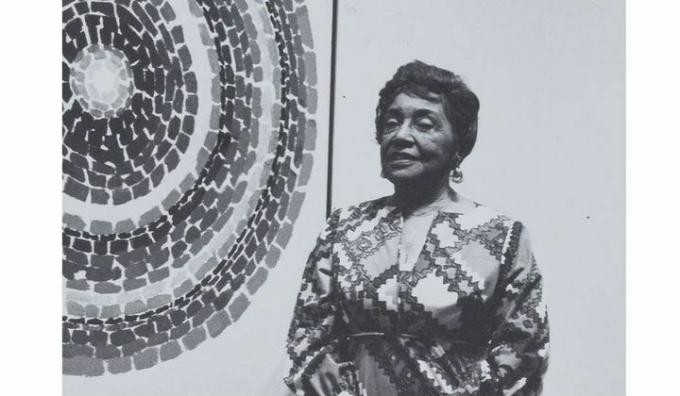 ασπρόμαυρη εικόνα της Alma Thomas μπροστά σε μια από τις αφαίμασεις του κύκλου της